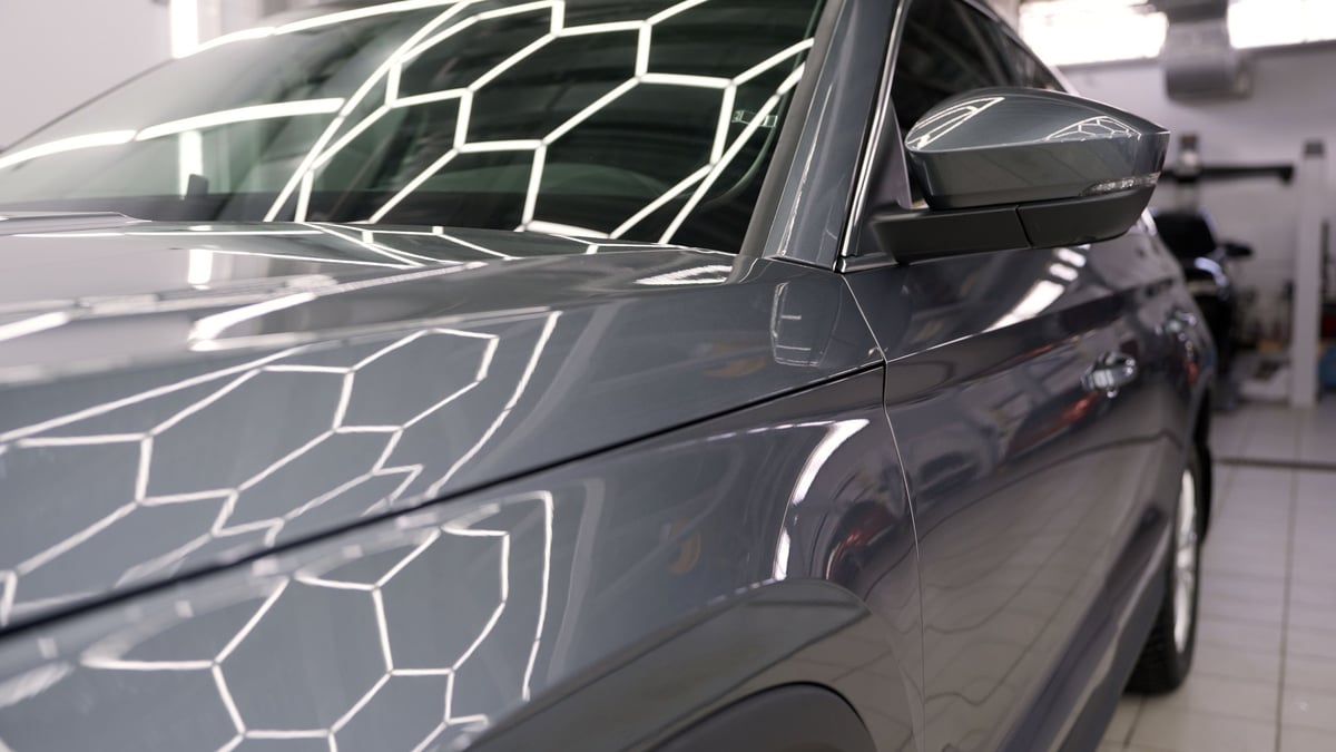 Detailer correcting black car paint under bright studio lighting for a mirror finish