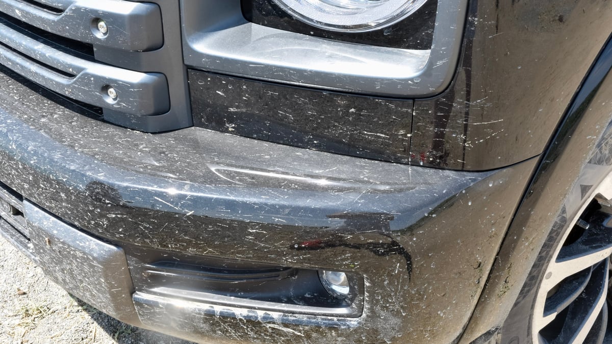 Mud-covered dark SUV front end after a road trip, glistening wet under studio lights