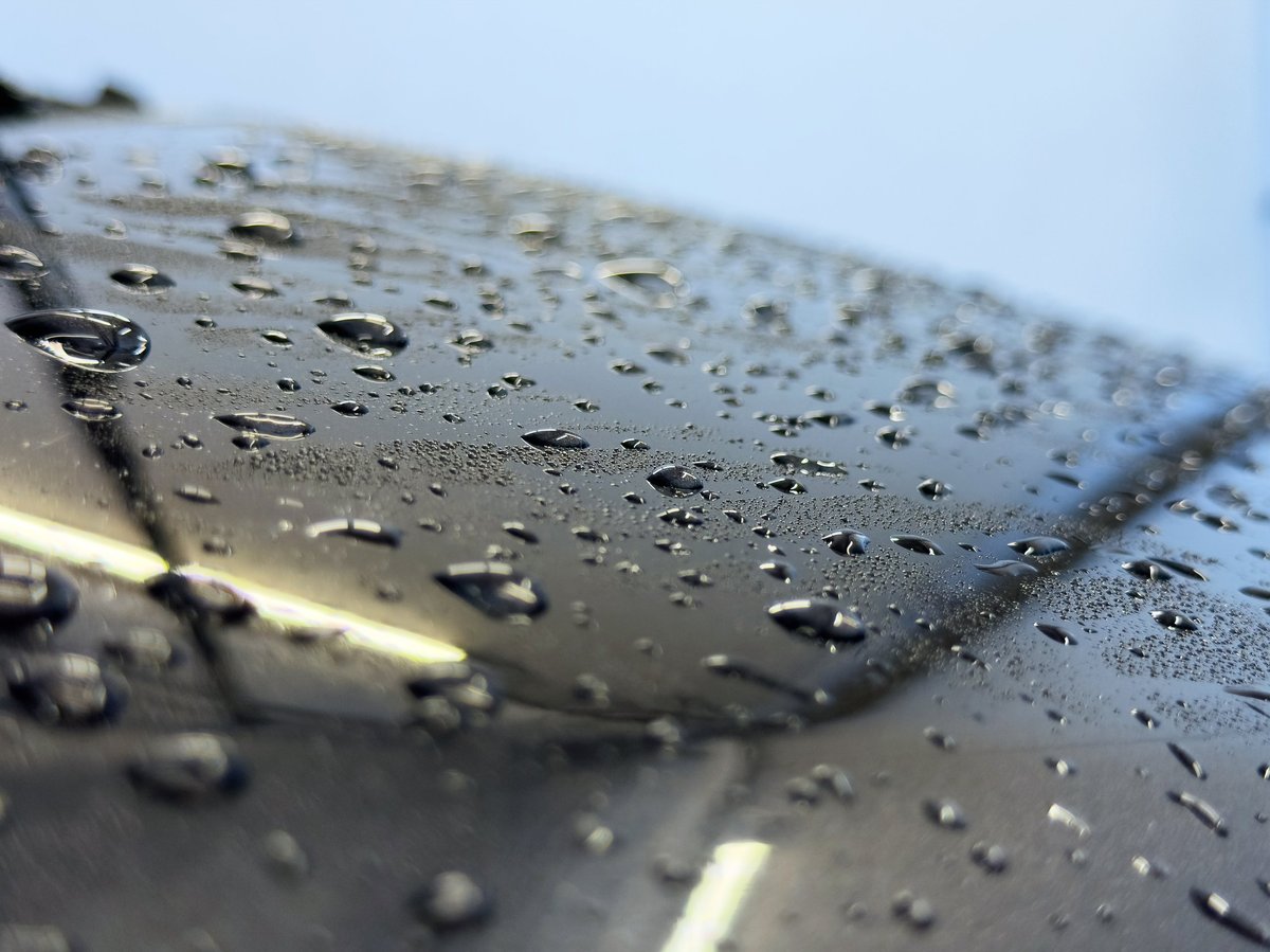 Macro close-up of water beading on glossy black car paint showing hydrophobic ceramic coating